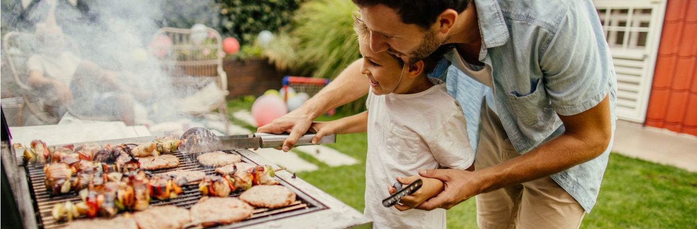 Father showing son how to cook food on a barbeque in a back garden