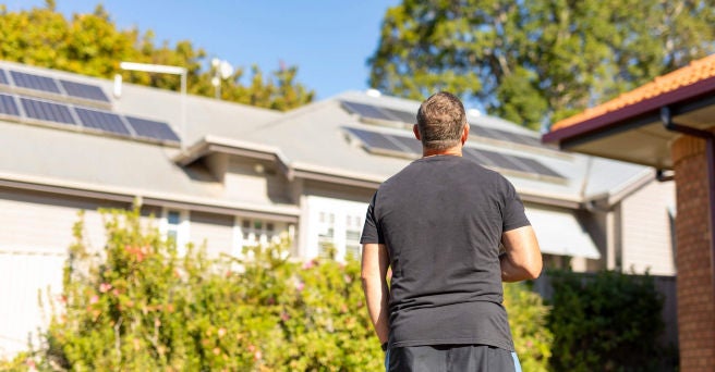 Back of a man drinking coffee and looking up at his solar installation on the roof