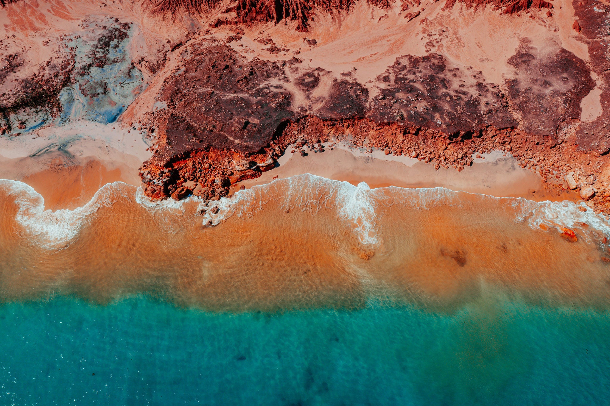 Aerial view of red desert cliffs with turquoise ocean lapping the beach