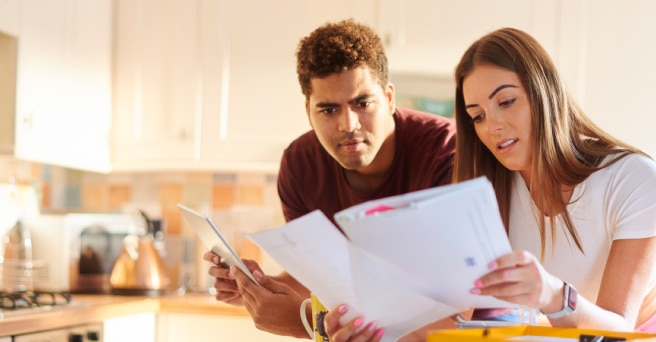 Couple in a kitchen reading a paper bill and looking concerned