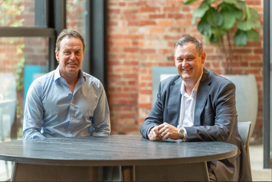 Tally CEO Andrew Duncan and Alinta Energy CEO and MD Jeff Dimery sitting a table together and smiling with a brick wall behind