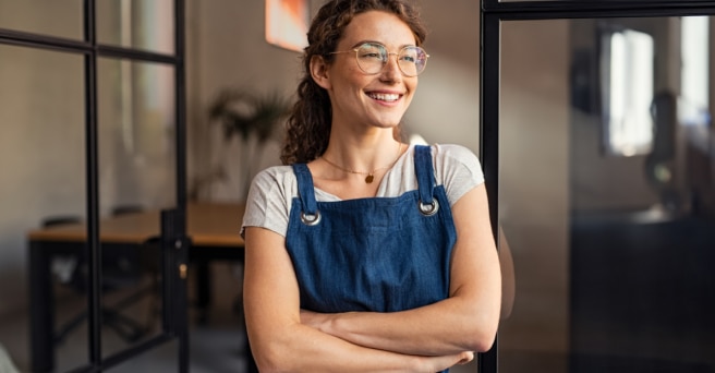 Woman in an apron with arms folded, smiling at shop door 