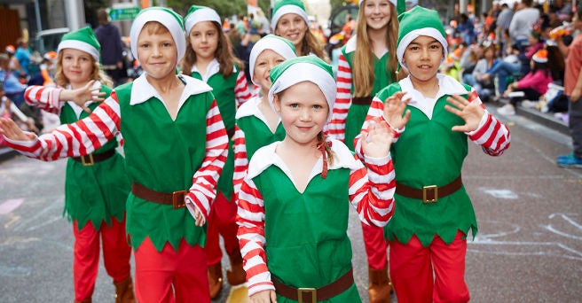 Group of smiling children dressed as elves waving to the camera and to the crowds