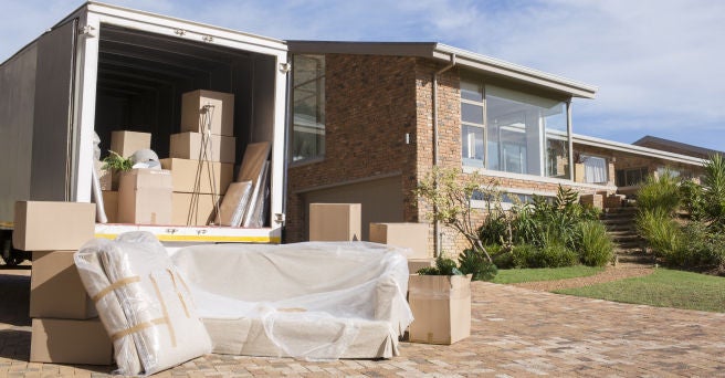 Open removals truck showing packing boxes inside and outside, parked on a driveway outside a house